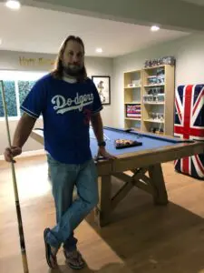A man with a Los Angeles Dodgers jersey standing next to a pool table